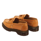 A pair of tan leather slip-on loafers with tassel details and dark brown soles, shown from a three-quarters angle on a white background.