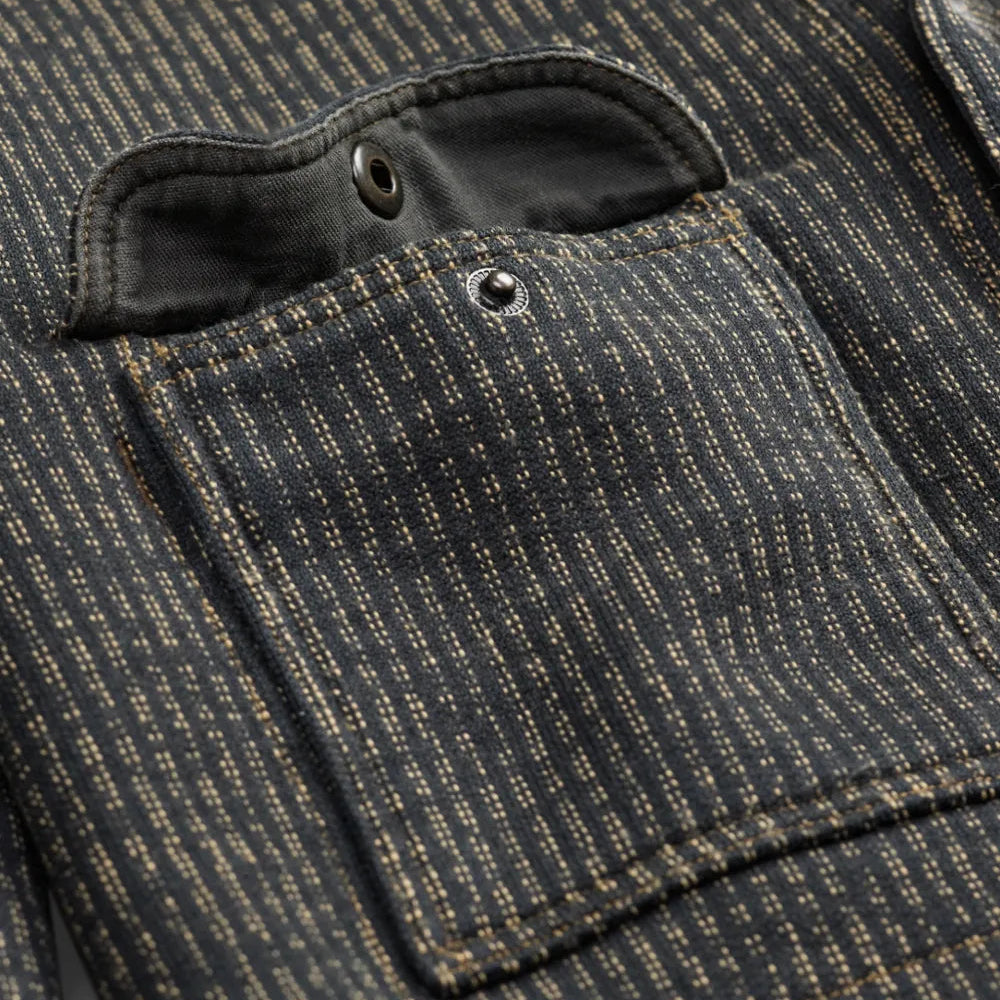 Close-up of a dark charcoal gray and black pinstriped fabric jacket pocket with a buttoned flap and a small metal rivet.