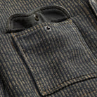 Close-up of a dark charcoal gray and black pinstriped fabric jacket pocket with a buttoned flap and a small metal rivet.