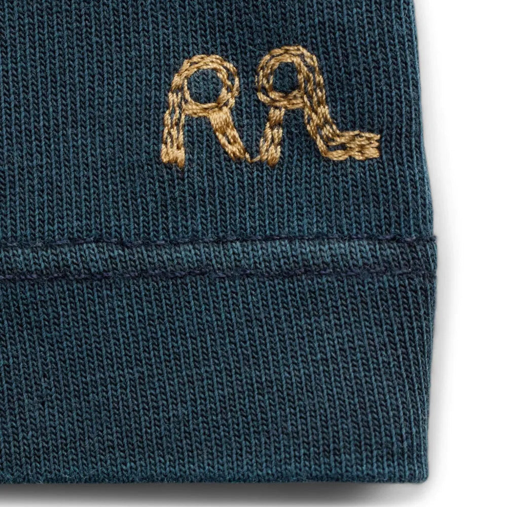 Close-up of a dark navy knit fabric hem with a gold embroidered monogram logo on the side.