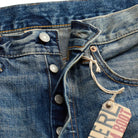Close-up of a blue denim jeans with a brand tag on a blue background