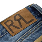 Close-up of blue denim jeans showing a brown leather patch with the stylized letters 'RRL' and part of a matching patch at the bottom right.