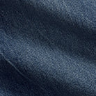 A close-up of dark blue denim fabric with visible twill texture and soft folds.