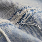 Close-up of light blue denim fabric with a distressed tear showing frayed white threads and visible twill weave texture.