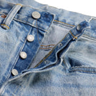 Close-up of a pair of light blue denim jeans showing the button fly, belt loops, and front pocket details.