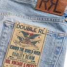 Close-up of the back pocket of light blue denim jeans showing a large vintage-style paper patch that reads 'DOUBLE RL' and 'RRL VINTAGE 5 POCKET,' plus a brown leather patch with 'RL' near the waistband.