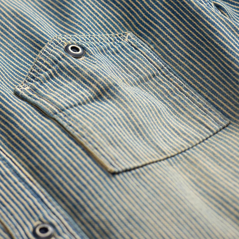 Close-up of a blue and beige striped shirt fabric with a chest pocket and metal snap buttons.