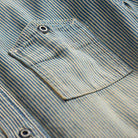 Close-up of a blue and beige striped shirt fabric with a chest pocket and metal snap buttons.