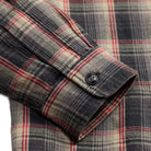 Close-up of a plaid flannel shirt cuff with a button, showing a pattern of dark gray, beige, and red.