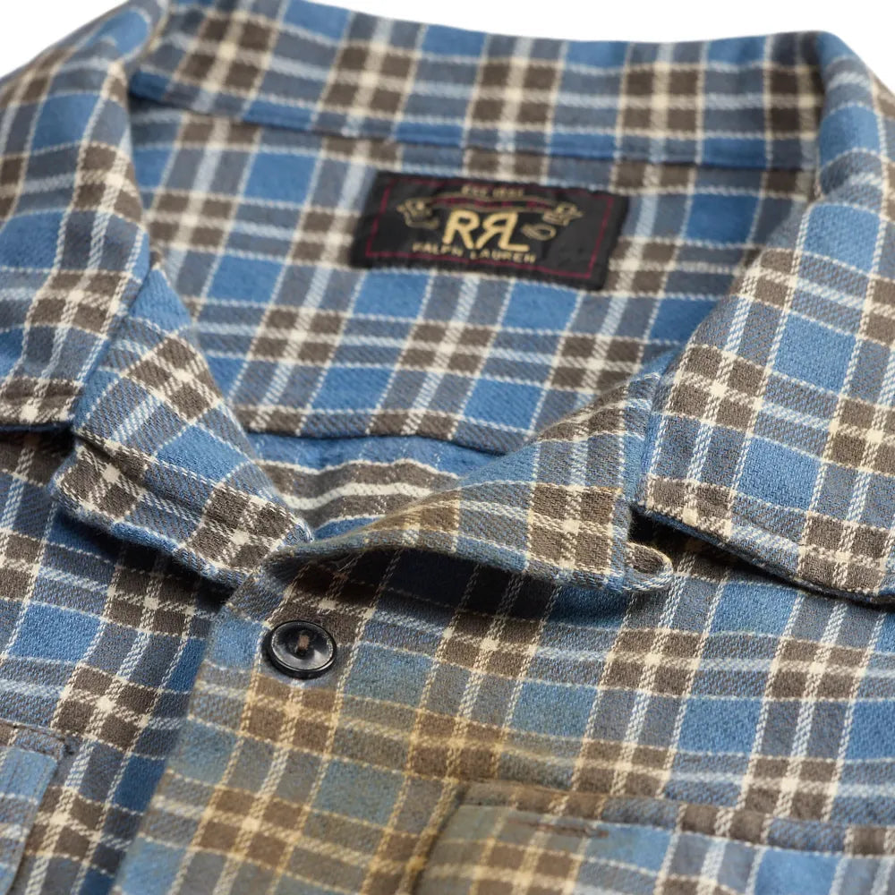 Close-up of a plaid button-up shirt with a blue, brown, and beige pattern, featuring a collar label with 'R.A.C' branding.