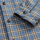 Close-up of a blue plaid button-down shirt with brown and white stripes, featuring dark buttons and a folded cuff.