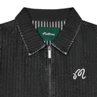 Close-up of a dark gray textured zip-up jacket with a pointed collar, featuring a green Malbon neck label and a white embroidered script 'M' on the chest.