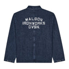 A dark blue ribbed denim jacket shown from the back, featuring 'MALBON IRONWORKS DVSN.' printed in distressed white block letters across the upper back.