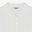 Close-up of a white textured knit polo shirt with a collar and white buttons, showing the 'Malbon' brand label inside the neck.