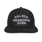 A black flat-brim baseball cap with white embroidered text reading 'MALBON IRONWORKS DVSN.' on the front, shown against a plain white background.