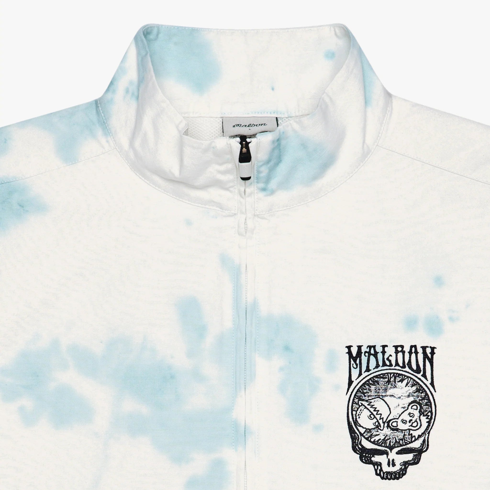 A close-up of a white and light blue tie-dye quarter-zip pullover jacket. The left chest features a black printed graphic of a Grateful Dead skull inside a circle with the word 'MALBON' above it.