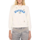 A woman modeling a cream-colored sweatshirt with 'MOTHER' written in blue letters across the chest, embellished with small stars and an eye motif against a plain white background.