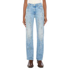 A model stands against a light gray studio background wearing light-wash blue jeans with small scattered rhinestone embellishments, a white top, and brown shoes.