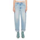 A woman modeling light-wash blue jeans with a cream crop top and green snakeskin boots, standing against a plain white background.