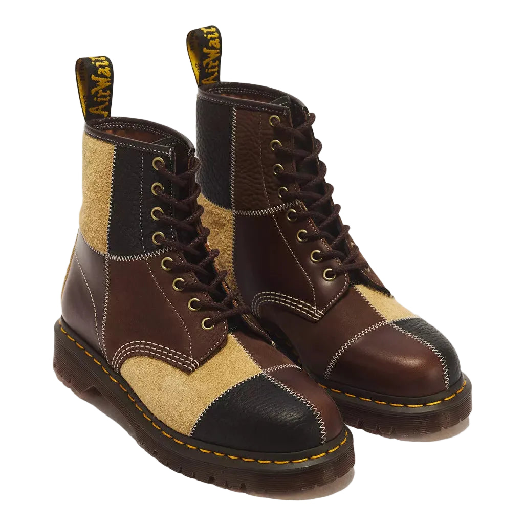 A pair of Dr. Martens patchwork boots in brown, beige, and black leather, featuring yellow stitching and pull tabs on a white background.