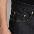 Close-up of a person wearing dark indigo denim jeans, showing the back pocket with contrast yellow stitching and silver metal rivets.