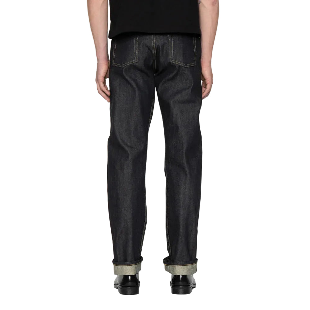 Rear view of a person wearing dark indigo denim jeans with rolled cuffs and black shoes, standing against a white background.