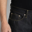Close-up of a person wearing dark indigo denim jeans with yellow contrast stitching, showing the back pocket and waistband area.