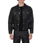 A man wearing a dark indigo denim trucker jacket over a black t-shirt and matching dark jeans, standing against a white background.