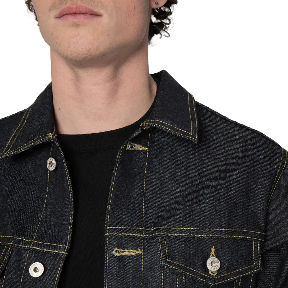 Close-up of a person wearing a dark indigo denim jacket over a black t-shirt, showing the collar, button, and chest pockets.