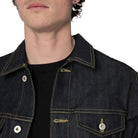 Close-up of a person wearing a dark indigo denim jacket over a black t-shirt, showing the collar, button, and chest pockets.