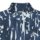 Close-up of a navy blue zip-up jacket with a white abstract paint-splatter pattern and a white script logo on the chest, set against a plain light background.