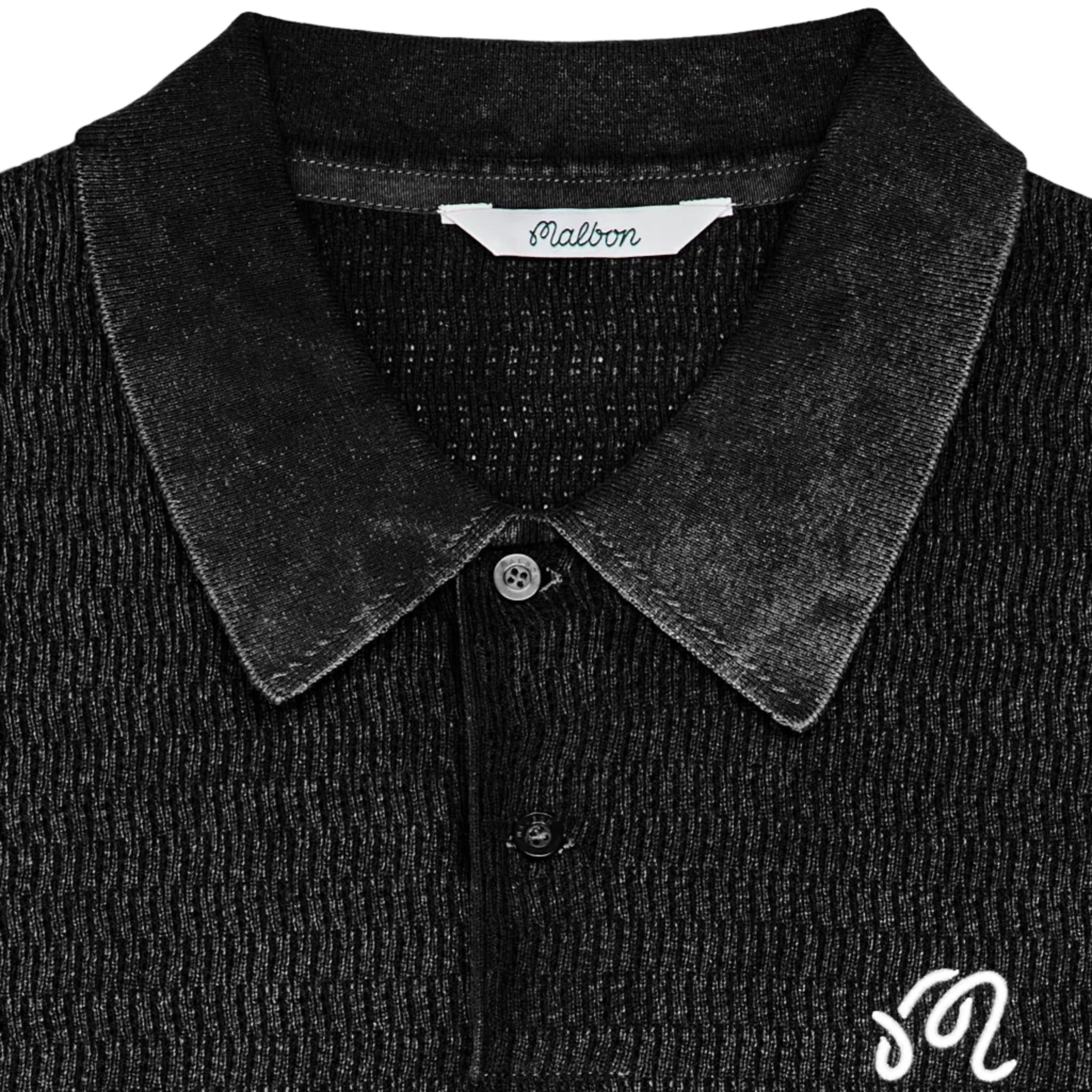 Close-up of a black ribbed knit polo shirt featuring a white embroidered monogram logo on the chest and a visible 'Malbon' brand label inside the collar.