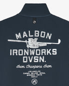 Close-up of the back of a dark navy textured polo shirt with a white distressed graphic reading 'MALBON IRONWORKS DVSN.' and additional text below, on a light gray background.