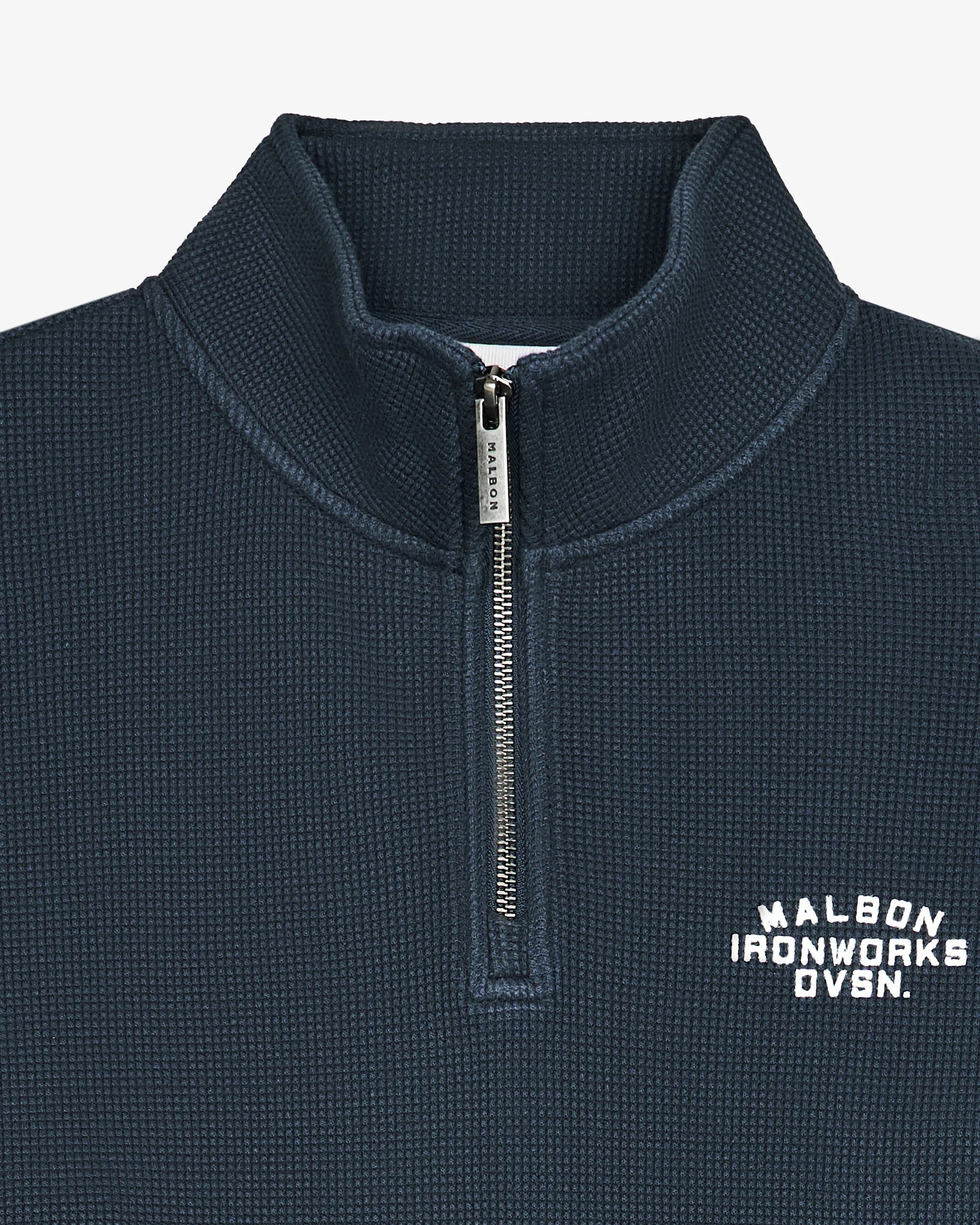 Close-up of a navy blue textured quarter-zip pullover with a white embroidered 'MALBOX IRONWORKS DVSN.' logo on the left chest and a silver zipper pull.