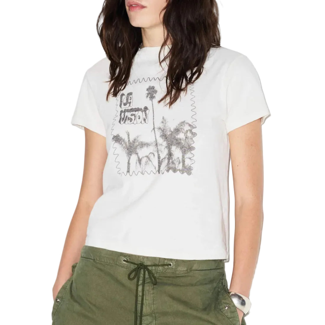 A woman wearing a white short-sleeve graphic t-shirt with a distressed black palm tree print, paired with olive green drawstring pants, against a plain white background.