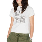A woman wearing a white short-sleeve graphic t-shirt with a distressed black palm tree print, paired with olive green drawstring pants, against a plain white background.