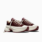 A pair of chunky low-top sneakers in burgundy and off-white, featuring a textured burgundy upper, white laces, and a thick white platform sole with burgundy outsole details, shown against a plain white background.