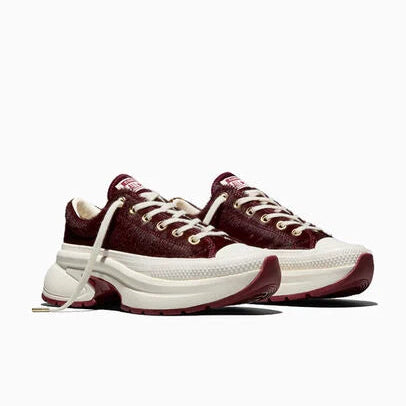 A pair of chunky low-top sneakers in burgundy and off-white, featuring a textured burgundy upper, white laces, and a thick white platform sole with burgundy outsole details, shown against a plain white background.