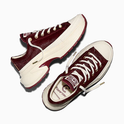 A pair of low-top sneakers shown from angled overhead views on a clean white background. The shoes feature a deep burgundy pony hair upper, chunky off-white platform soles, white laces, and a small gold-tone logo detail on the side.