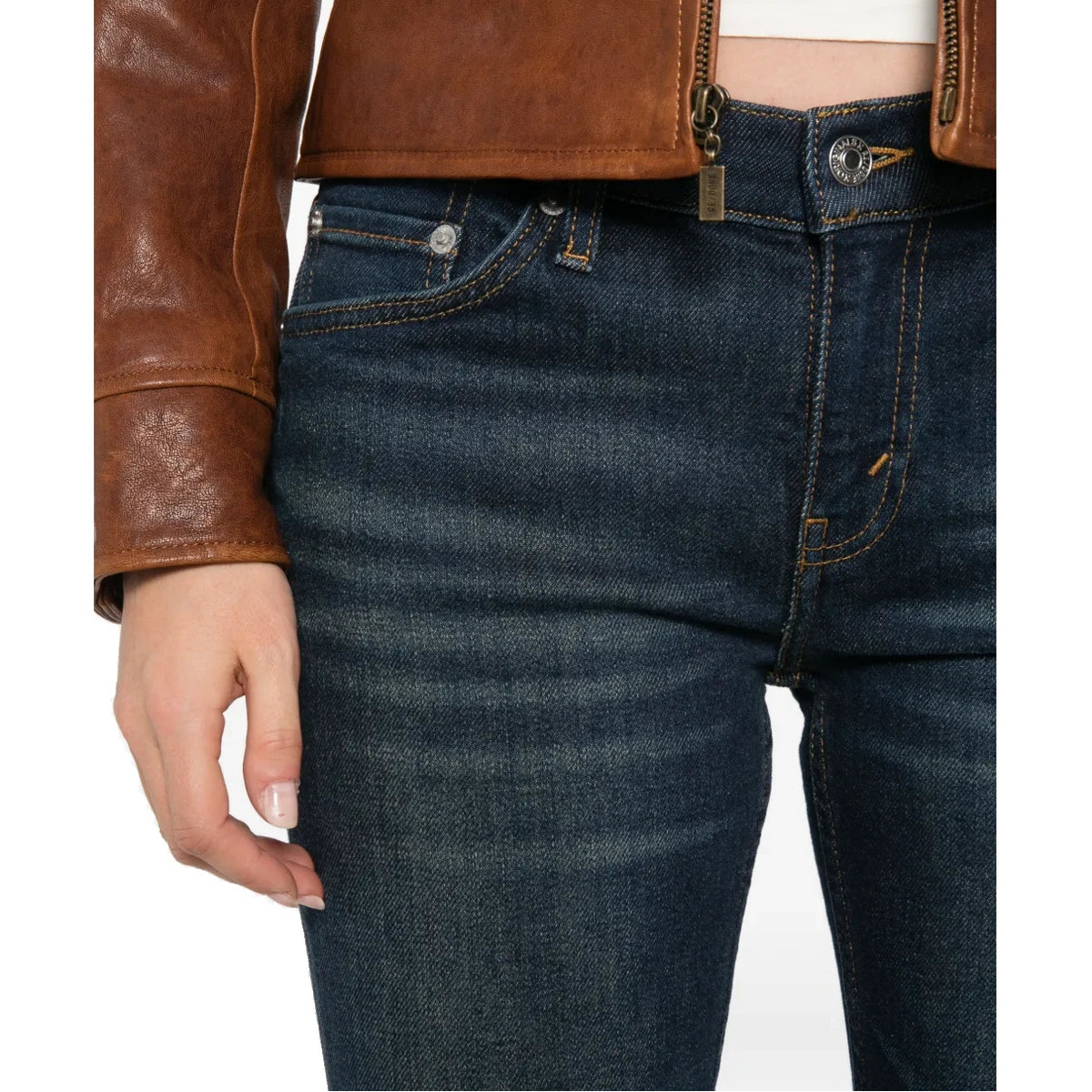 Close-up of the Micro Boot Jean’s front waistband, showing the metal button, coin pocket and contrast stitching, worn with a brown leather jacket.