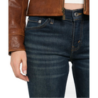 Close-up of the Micro Boot Jean’s front waistband, showing the metal button, coin pocket and contrast stitching, worn with a brown leather jacket.