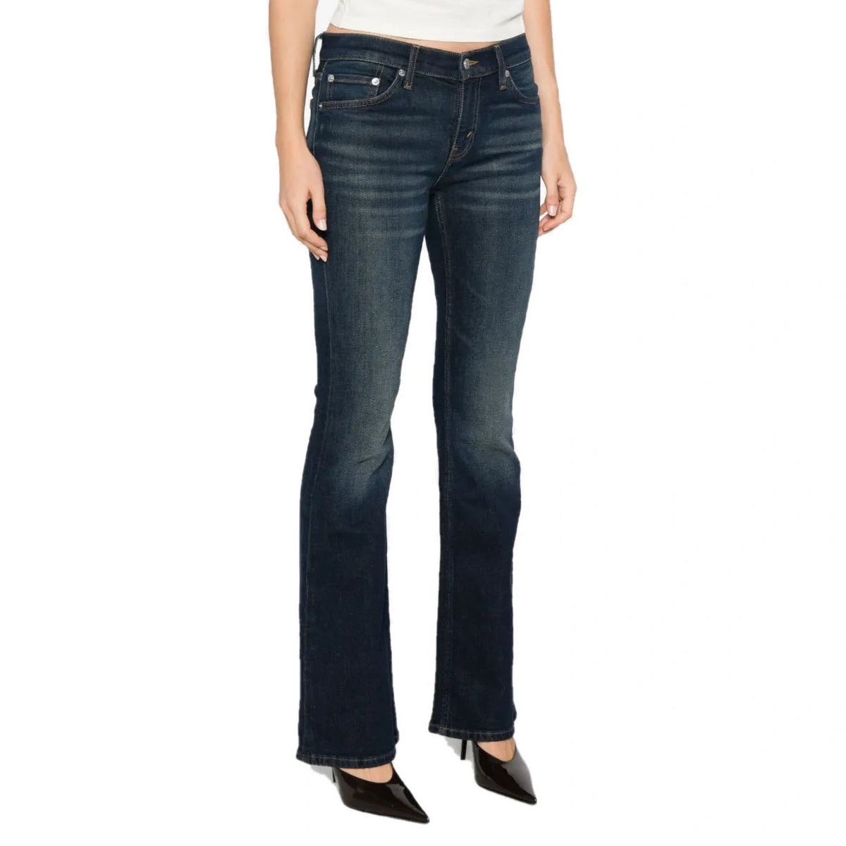 A model wears the dark indigo Micro Boot Jean with a white cropped top and black pointed heels, seen from a three-quarter angle.