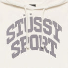 Close-up of a cream-colored hoodie featuring a large gray arched 'STUSSY SPORT' logo printed across the chest, with white drawstrings.