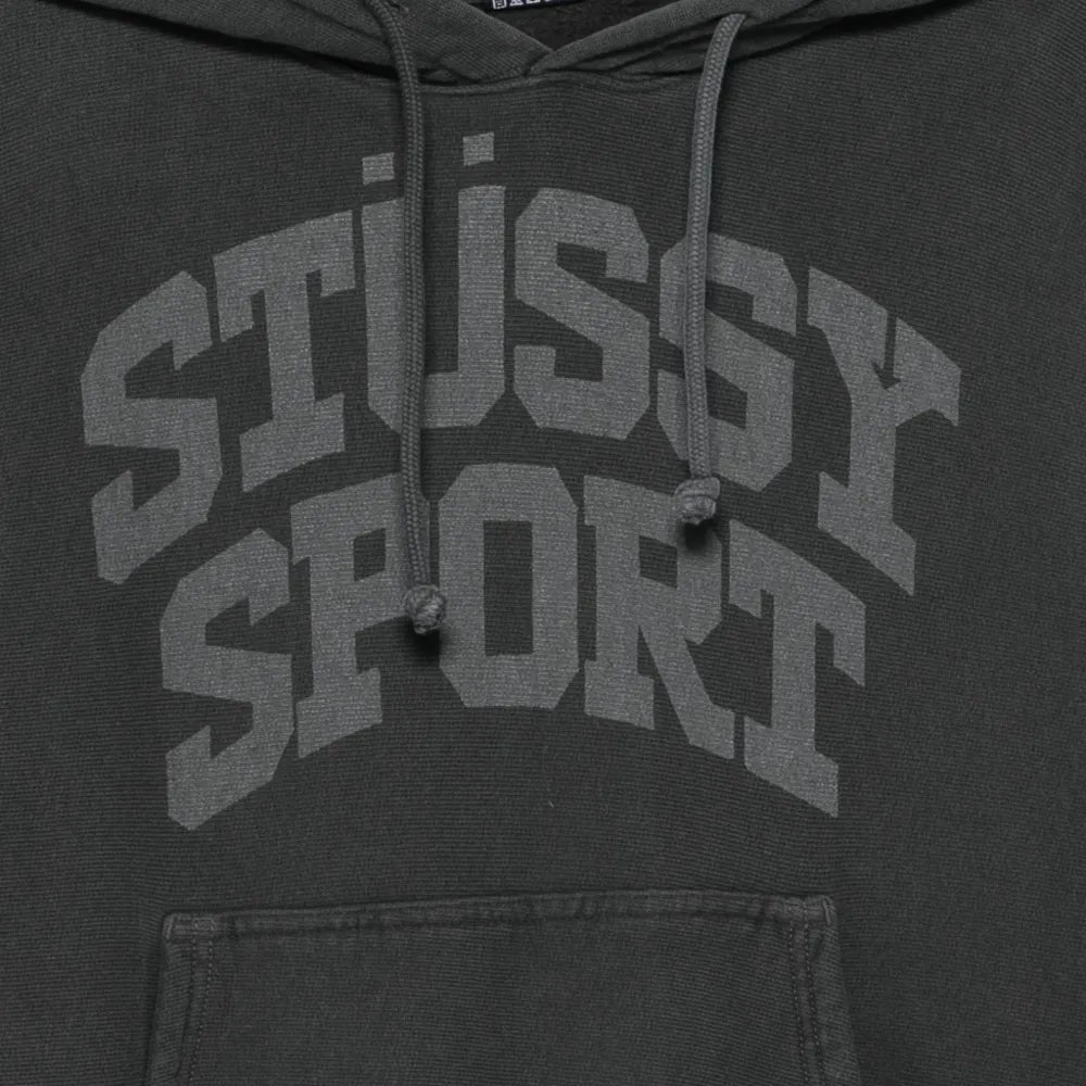 Close-up of a dark charcoal gray hoodie featuring a large, tonal gray 'STUSSY SPORT' graphic printed across the chest, with matching drawstrings and a front kangaroo pocket.