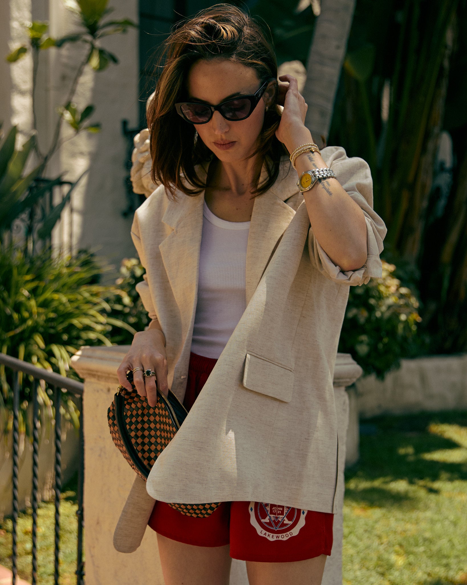 Woman in a beige blazer and red shorts standing outdoors with plants in the background
