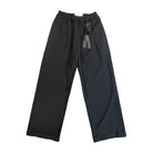 Front view of black wide-leg Song For The Mute pants laid flat. They have an elastic drawstring waist with long rope cords and a carabiner key charm with an “A” tag hanging from a belt loop.