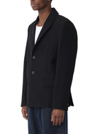 Man wearing a black blazer and blue pants on a white background