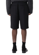 Person wearing a dark gray textured sweater and black shorts on a white background