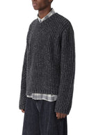 Man wearing a dark textured sweater and wide-leg jeans on a white background