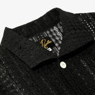 Close-up of a black textured shirt with a brand logo on a white background